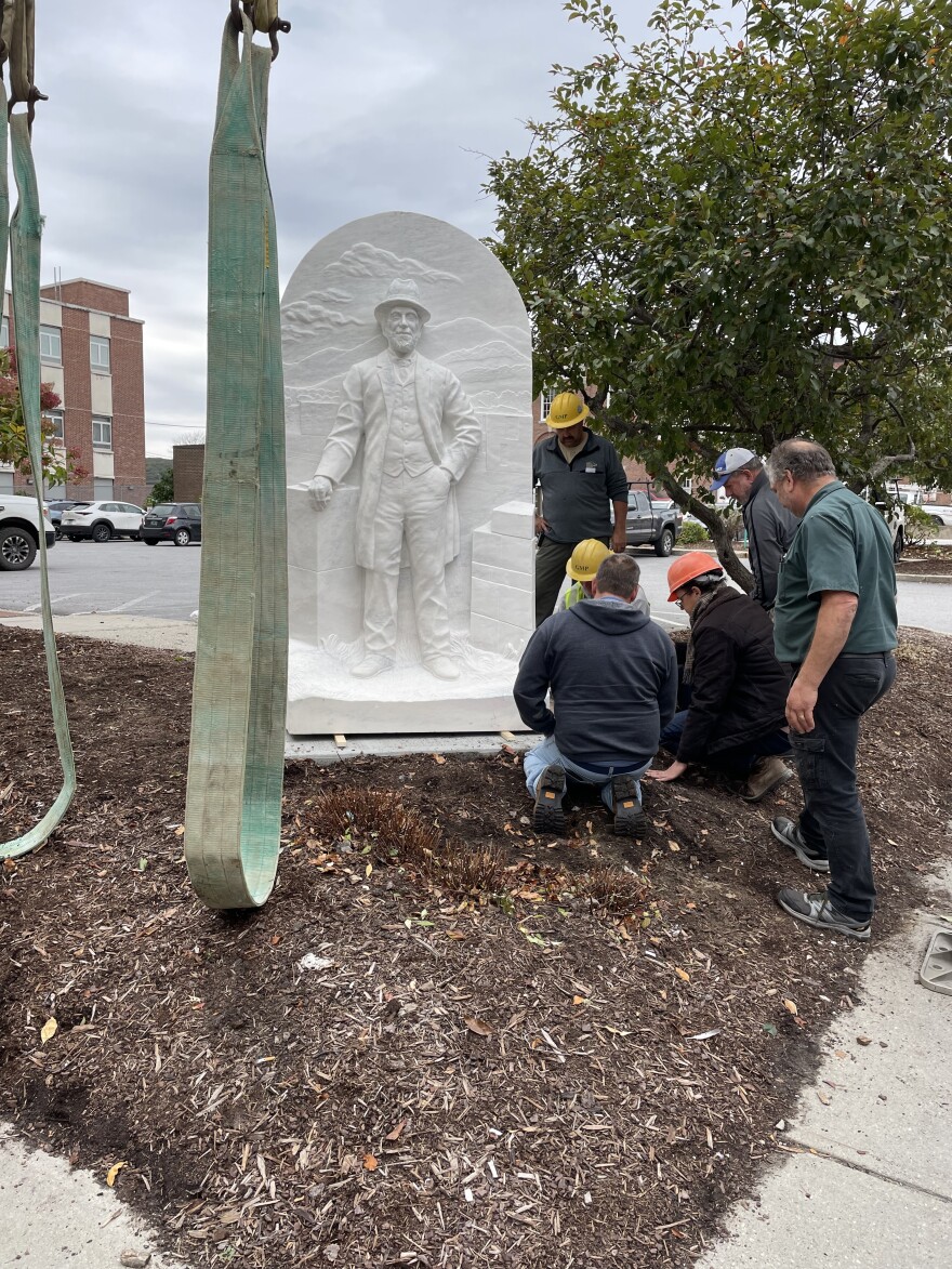 Workers near a marble sculpture showing a man with mountains behind him and blocks of marble next to him 