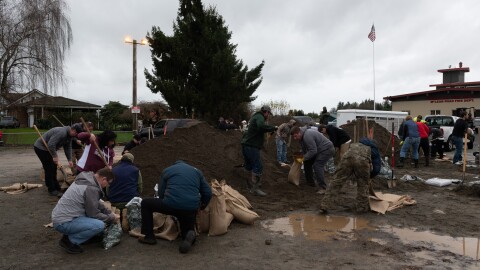 A group of people with shovels fill bags with dirt on an overcast day.