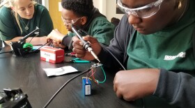 Three people sit at a table building air quality monitors.