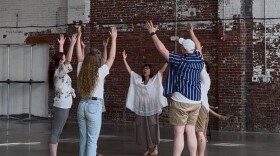 Seven people stand in a circle with their hands in the air.