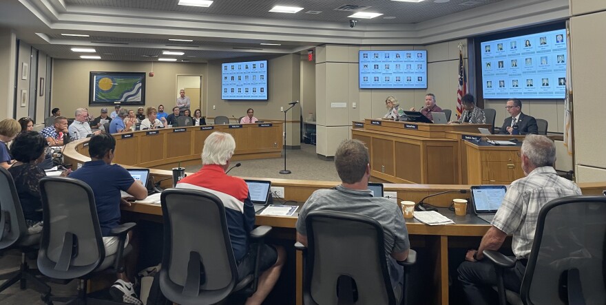 A horse shoe of county board members sit facing a large desk. 