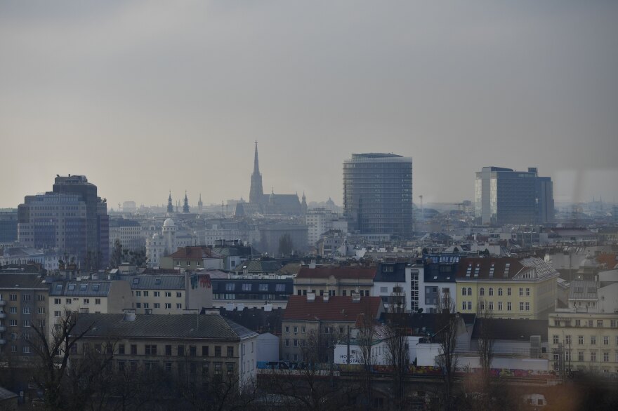 The Vienna skyline includes red and yellow buildings in front of gray high rises.