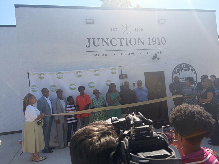 City leaders and members of Junction 1910 stand behind a ribbon. Juction 1910 is written on the building above them.