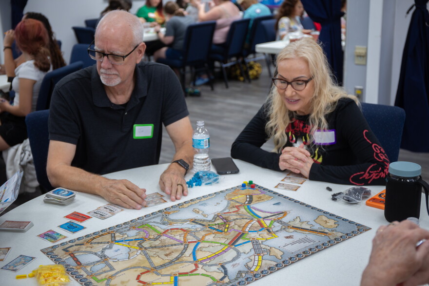 Two older people with a board game on the table in front of them.