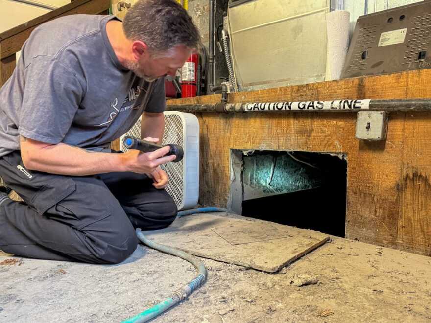 Gavin Ockerman shines a light into a crawl space under their home in Butte where river water flooded on June 21, 2025.