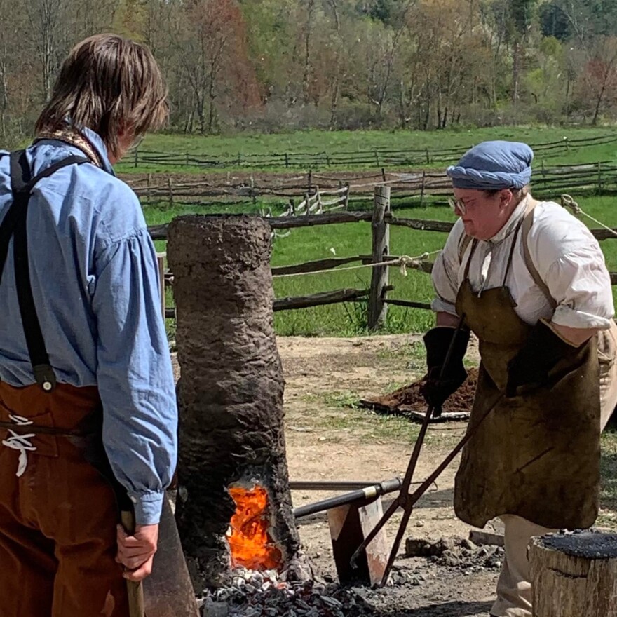 Using a pair of tongs, Hale removes smelted iron from a furnace to be worked.