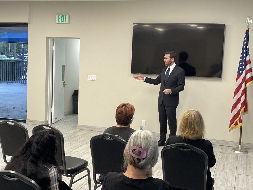 A man in a suit speaks to a small gathering of seated people