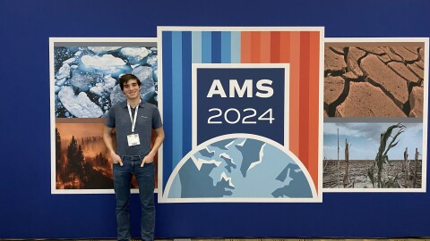 UD Student Thomas Florio stands in front of an AMS sign poster wall