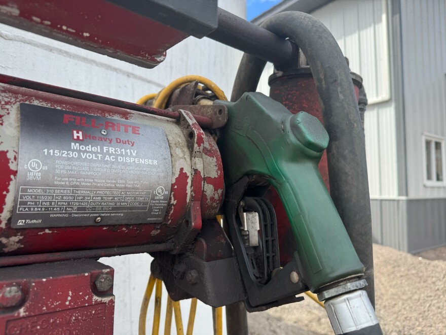 A green gas handle attached to a large, white, cylindrical gas tank is exposed to the open air. 