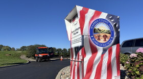 A ballot drop box designed to look like an American flag sits in a black asphalt parking lot.