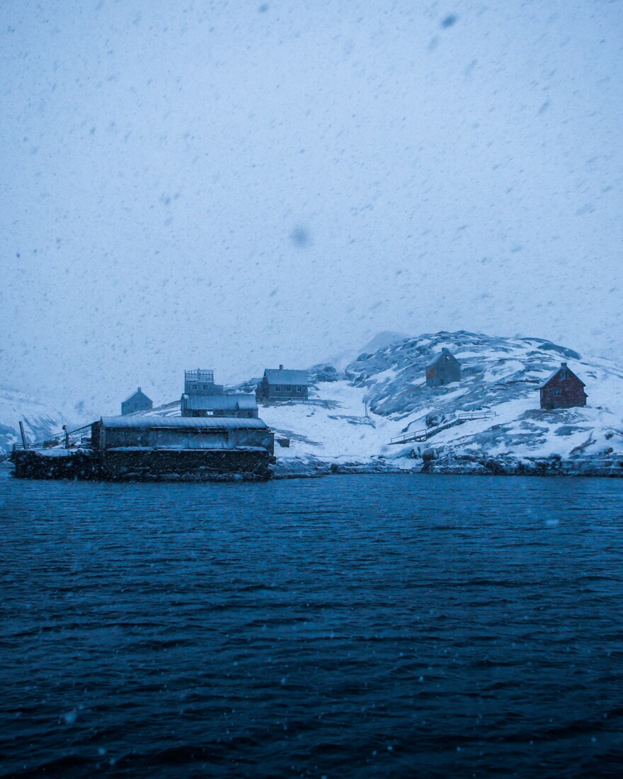 Kangeq's old wharf and houses appear ghostlike through a late winter snowstorm.