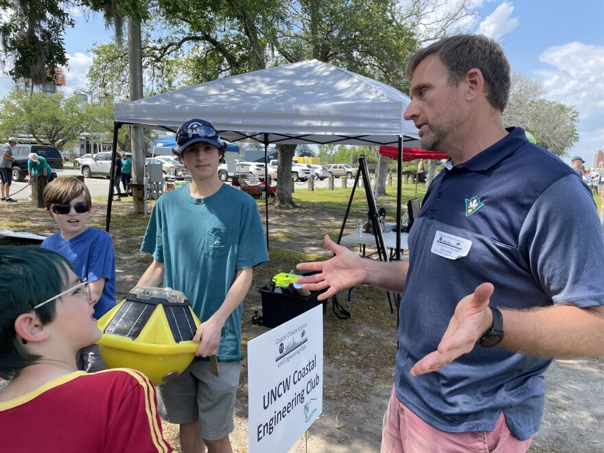 Professor Joe Long, right, and student Noah Johnson, holding a bouy, explain how the fixture can measure numerous indicators in the ocean to a group of children.