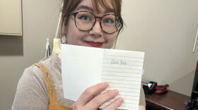 A woman in a yellow dress holds up a small notebook opened to a page that says, "Ghost Book."