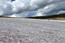 Two researchers stand on a vast ice patch in Wyoming’s Beartooth Mountains beneath large, dark clouds.