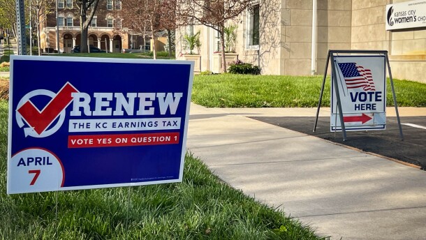 A blue sign with white and red lettering reads "Renew the KC earnings tax. Vote yes on question 1." Another in the background says "vote here"