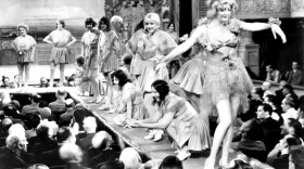 A black and white photograph showing a scene from the 1929 movie Applause directed by Rouben Mamoulian, featuring several showgirls performing on a raised stage before a seated theater audience.