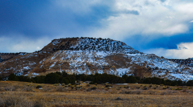 A small, rocky peak with some snow on it in an arid landscape.