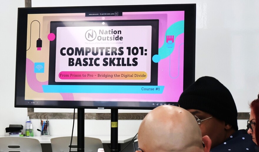 A group of peer navigators at Nation Outside around a table with a TV screen that says "Computers 101: Basic Skills". 
