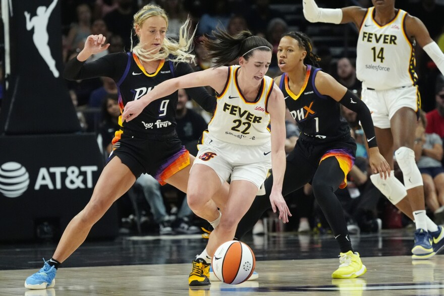 Indiana Fever guard Caitlin Clark (22) is defended by Phoenix Mercury guards Sophie Cunningham (9) and Sug Sutton (1) during the second half of a WNBA basketball game Sunday, June 30, 2024, in Phoenix.