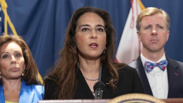 A woman in a jacket speaks at a podium.