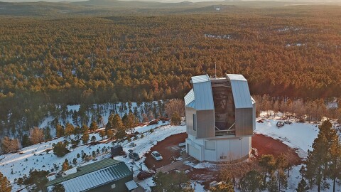 An aerial view of an open telescope dome surrounded by pine forest. 