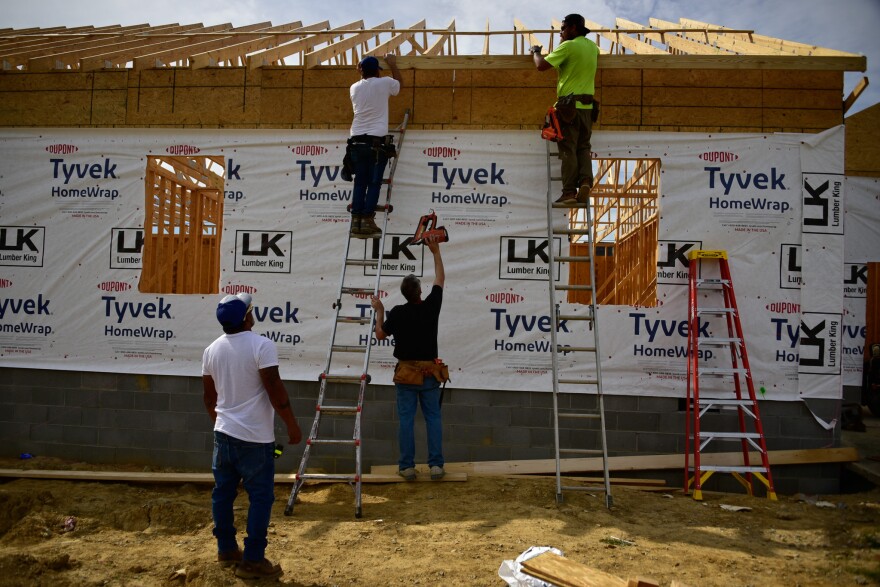 Hector Merced directs workers from the ground as his team nails a fascia board to a house they have just completed framing on.
