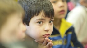 Young boy in classroom with brown hair has hands clasped 
