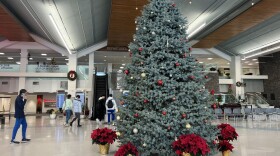  A decorated Christmas tree with red and gold ornaments sits in front of two escalators. 