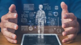 Hands on table looking as if holding a holographic image of digital symbols and shape of a person with circuitry lights