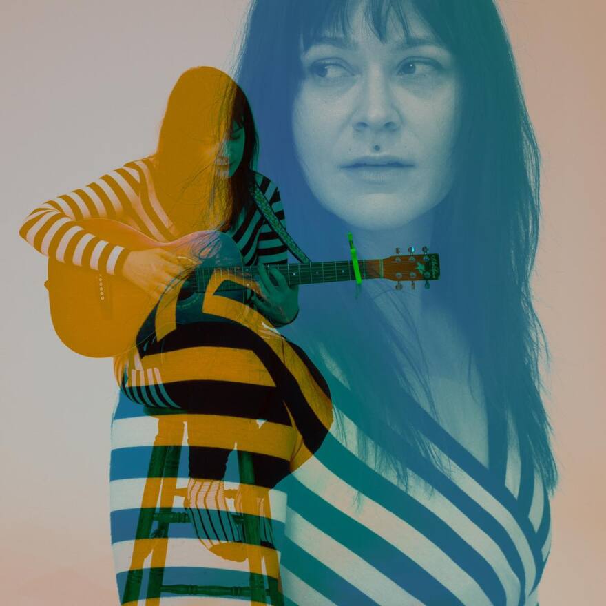 Two images of Silver Reeds imposed over each other with blue and yellow hues. One photo is her sitting on a stool and playing a guitar. The other is her standing to the left and looking over her right shoulder.