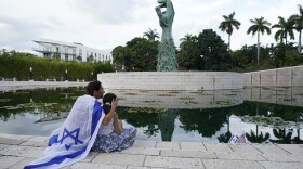 FILE - Draped in an Israeli flag, Elinor Ben David, left, hugs her daughter Liel Abissidan, 8, as they wait for a rally in support of Israel to start, at the Holocaust Memorial Miami Beach, Oct. 10, 2023, in Miami Beach, Fla. An estimated 525,000 Jews live in Miami's metropolitan area according to the American Jewish Population Project at Brandeis University. In South Florida, rabbis and community leaders are pushing their congregations to call their lawmakers and insist they back Israel as it ramps up its offensive.