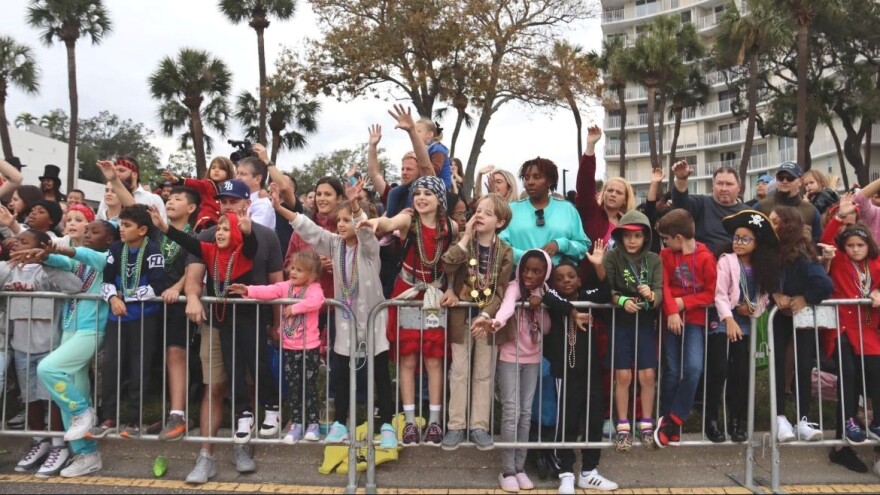 A line of children pressing up against metal barricades as they watch a parade.