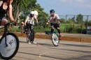 Three people riding bicycles carrying small mallets chase a ball while playing a game of hardcourt bike polo. 