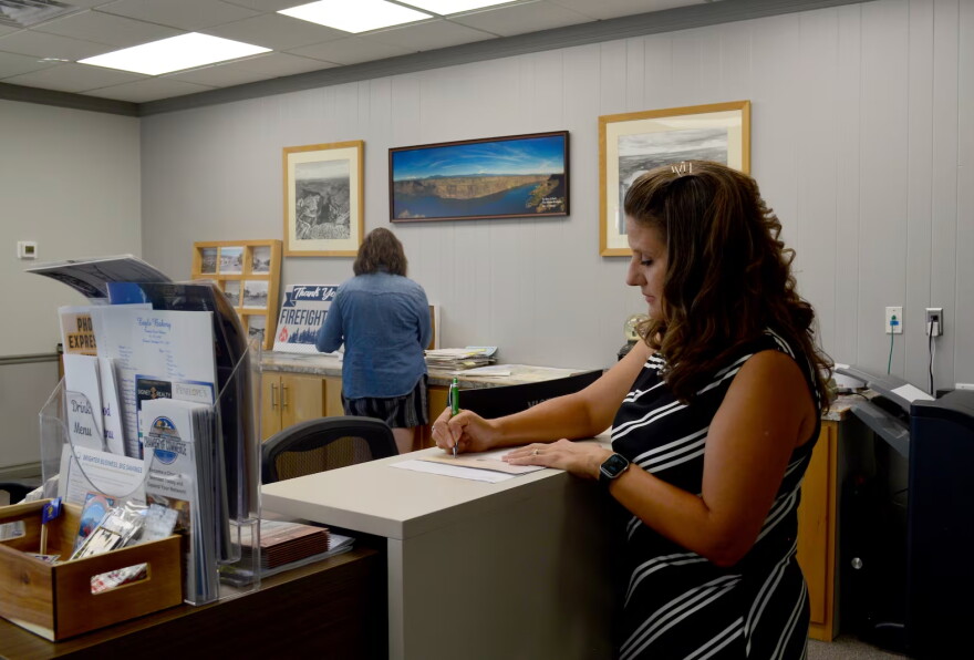 A woman in an office stands at a tall desk and writes on a piece of paper