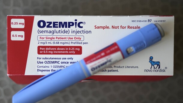 a blue pen-like injectable drug sits on top of a white and red box 
