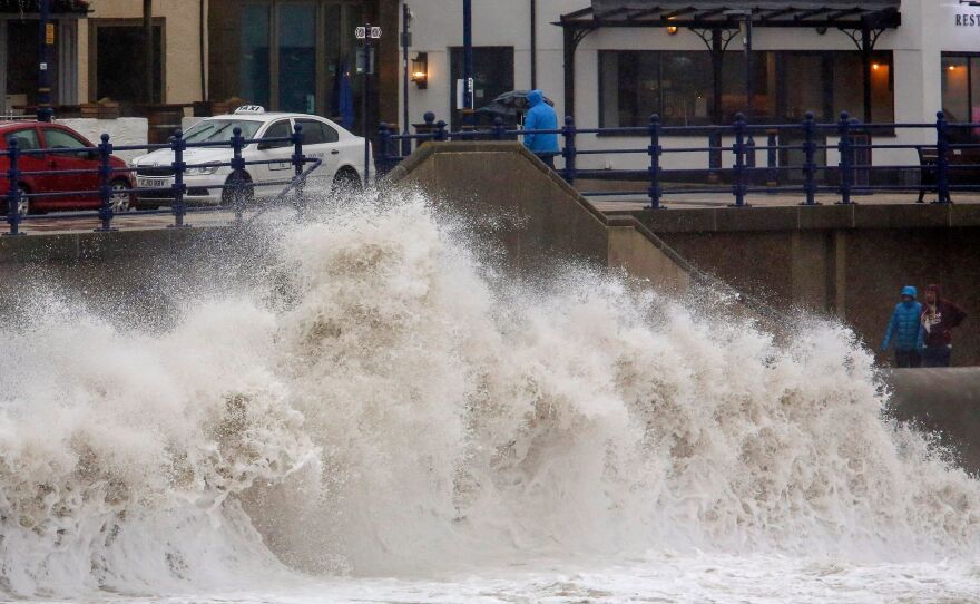 Pedestrians walk along the promenade as huge waves crash against the sea wall at Porthcawl, Wales, as Storm Dennis hits the U.K. on Saturday.
