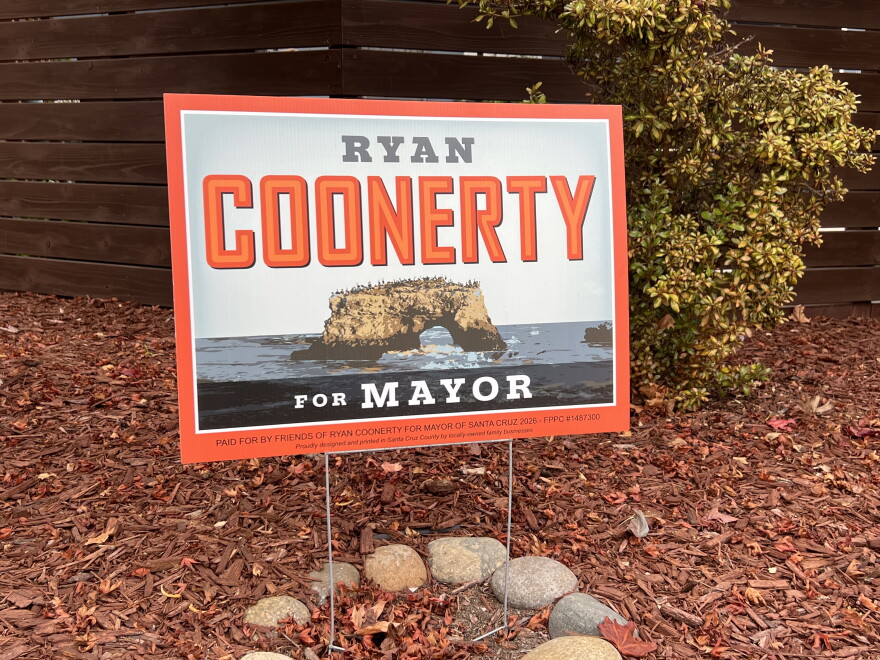 A square sign stands in a patch of dirt covered in wood chips. A bush and fence are behind it. 