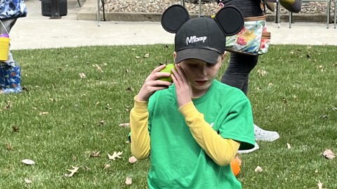 A child kneels on the ground and holds a beeping egg up to his ear that he just found.