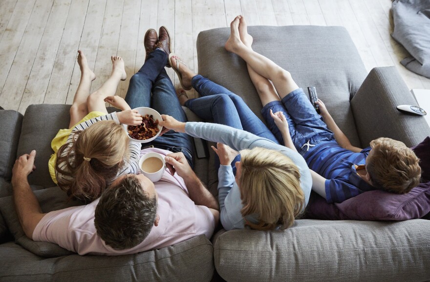 Parents and their two children seated on a sofa together. (Getty)
