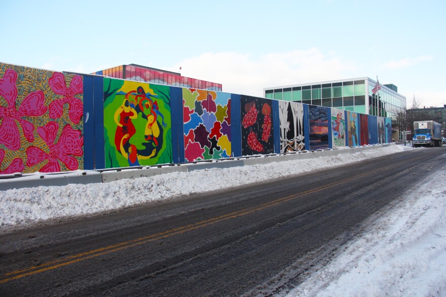 A series of colorful paintings cover a fence along a slushy road. 