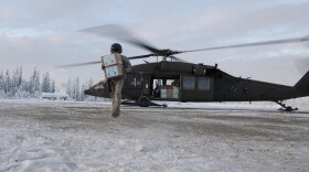 A masked man carries a box on a snoowy ground from his helicopter