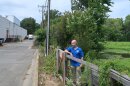 Rickie White, a bald white man in a blue shirt, looks out at the back lot of a shopping center, directly adjacent to the green wetland of Beaver Marsh.