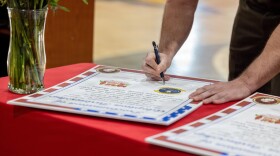 U.S. Marine Corps Lt. Col. James P. Psyhogis, commanding officer, Center for Naval Aviation Technical Training Unit New River, signs the adoption proclamation during an Adopt-a-School ceremony at Jacksonville High School in Jacksonville. The final adoption ceremony between Jacksonville High School and the Center for Naval Aviation Technical Training Unit New River marked a significant achievement for Onslow County School District as it reached a 100 percent adoption rate by various units of Marine Corps Installations East and II Marine Expeditionary Force in the Adopt-a-School program.