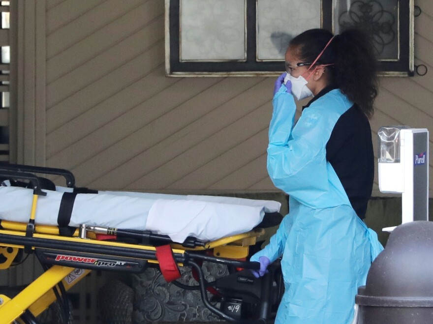 An ambulance worker adjusts her protective mask as she wheels a stretcher into a nursing facility in Kirkland, Wash., on Saturday where more than 50 people were found to be sick and are being tested for COVID-19 virus. [Elaine Thompson / AP]