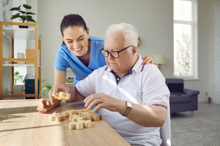 Nurse in retirement home helping old male patient with puzzle. 