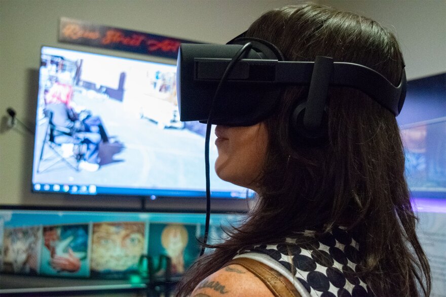 A women wears a black headset in front of a large TV. 