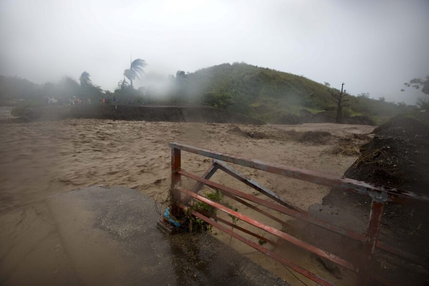 People watch from the other side of the La Digue river as water roars past the destroyed Petit Goave bridge, as Hurricane Matthew passes over, in Petit Goave, Haiti, Tuesday, Oct. 4, 2016. Hurricane Matthew slammed into Haiti's southwestern tip with howling, 145 mph winds destroying the bridge and cutting off road communication with the worst hit areas. ( AP Photo/Dieu Nalio Chery)