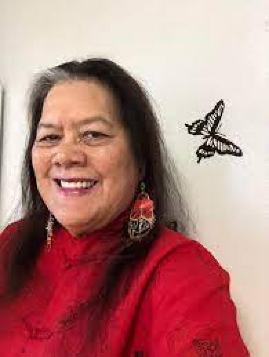 Hedy Tripp has long black hair and is wearing a red sweater and feather earrings.