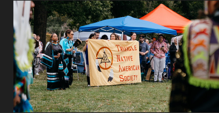 Women holding a banner that reads "Triangle Native American Society" surrounded by tribal members