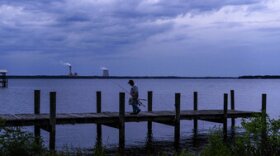 A fisherman walks along a dock on the St. Johns River as a coal-fired power plant stands in the background, in Palatka, Fla., Wednesday, April 14, 2021. After months in a prison cell, Warren Williams longed to fish the St. Johns again. He looked forward to spending days outdoors in his landscaping job, and to writing poems and music in his free time.